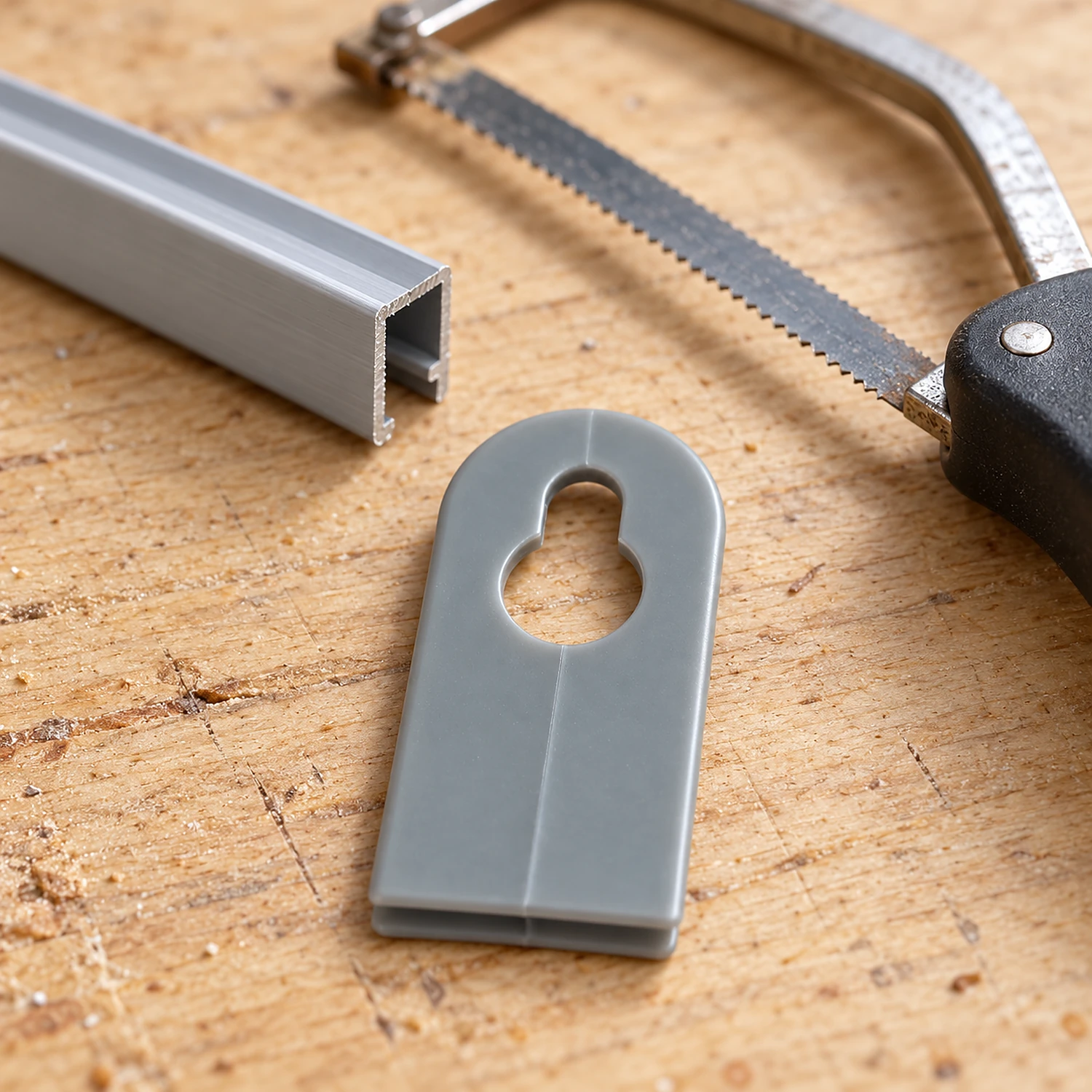 Grey closed hook on a workbench beside a rail offcut and a hacksaw