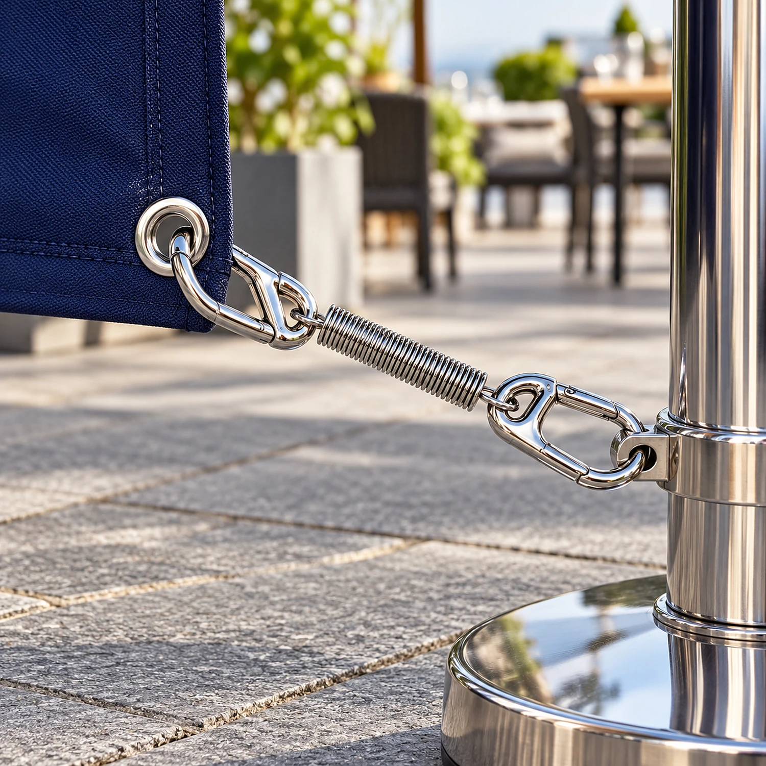 Chrome spring clip linking a barrier panel eyelet to its post on a hotel terrace